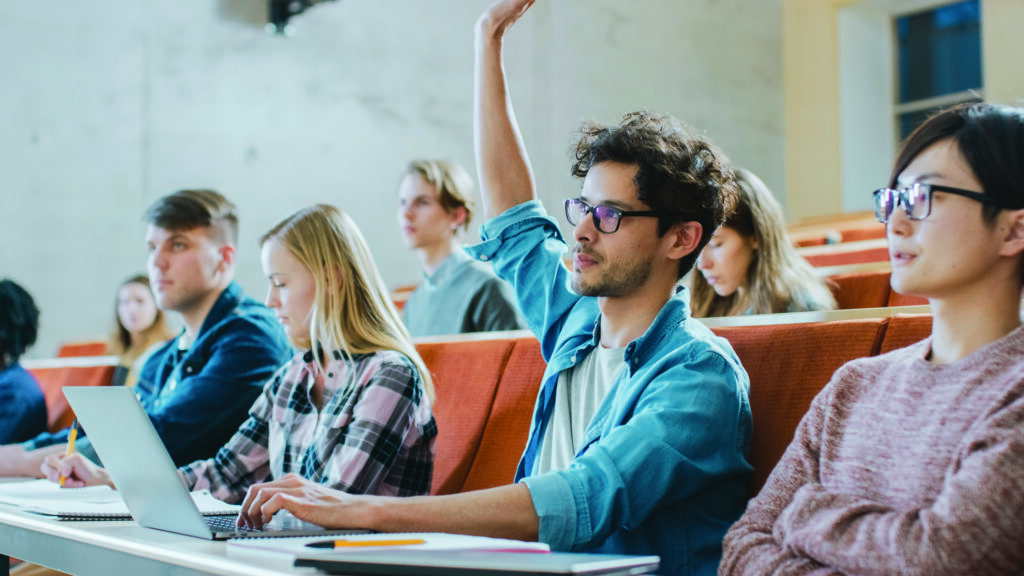 Handsome Hispanic Student Uses Laptop while Listening to a Lecture at the University, He Raises Hand and Asks Lecturer a Question. Multi Ethnic Group of Modern Bright Students.; Shutterstock ID 1077839366; purchase_order: License; job: Rugby World Cup Promo; client: Collingwood; other: